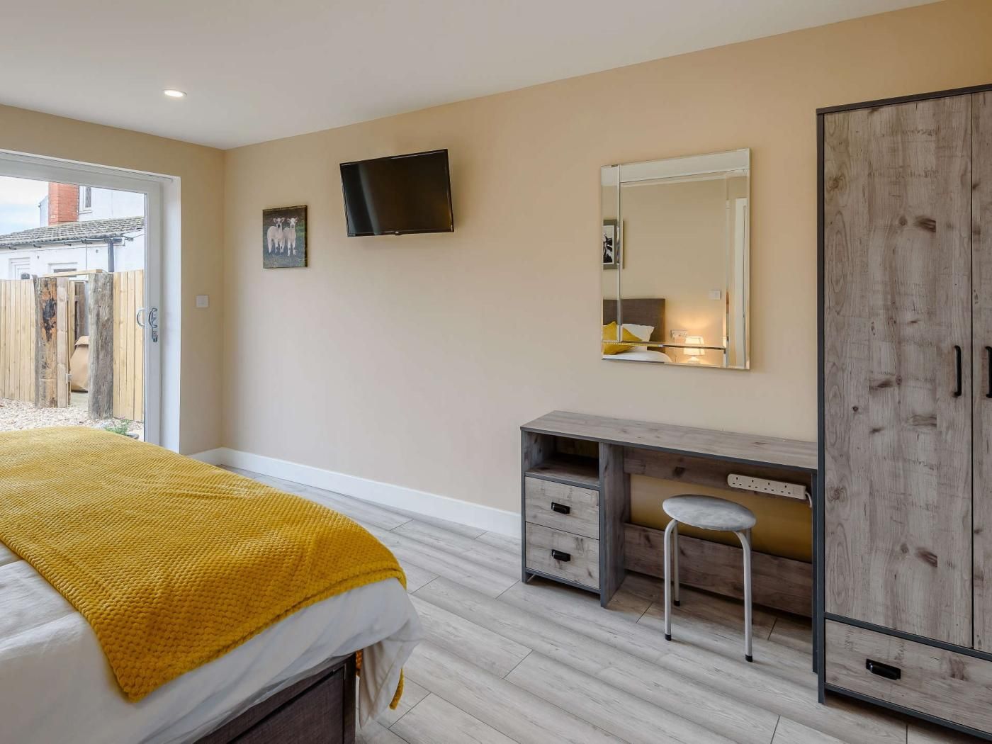 A bedroom with a bed, a desk, a mirror, and a wardrobe.