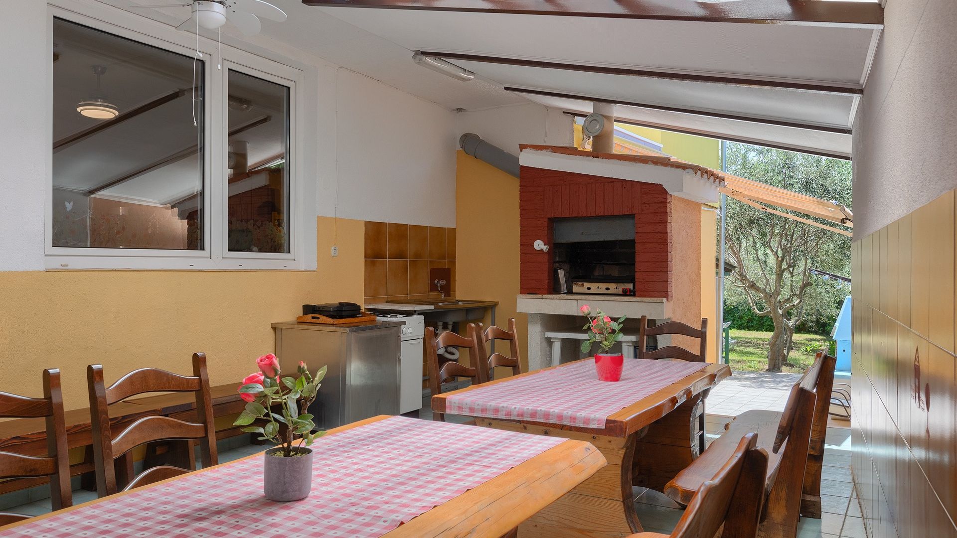 Une cuisine équipée d’un barbecue intégré, de chaises en bois et d’une table recouverte d’une nappe à carreaux.
