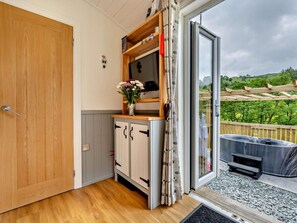 A room with a wooden door, a small cabinet, a mirror, and a view of a hot tub and garden outside. - 1 Bed in Penrith (oc-85531) (Deepdale)