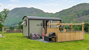 A caravan with a covered outdoor area, a small seating area, and a stone wall in a grassy field with mountains in the background. - 1 Bed in Penrith (oc-85531) (Deepdale)