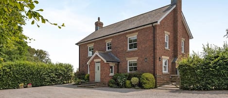 Une maison à deux étages, construite en briques, avec une entrée à l’avant, une allée et un jardin bien entretenu.