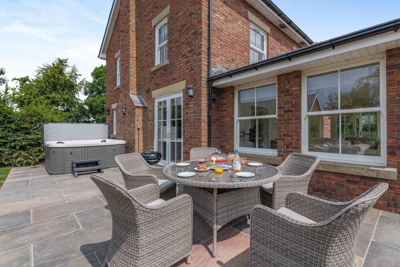 A patio with a dining table, wicker chairs, and a barbecue grill.