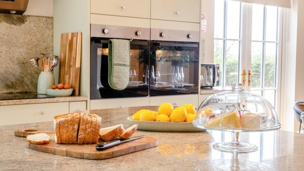 Une cuisine dotée d’un plan de travail en granit, d’une planche à pain, d’un bol de citrons et d’une vitrine contenant des produits alimentaires.