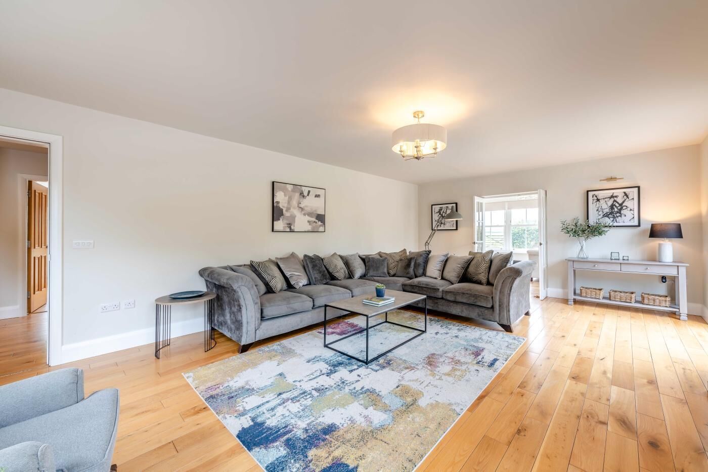 A modern living room with a grey sectional sofa, a coffee table, a console table with baskets, and a chandelier.