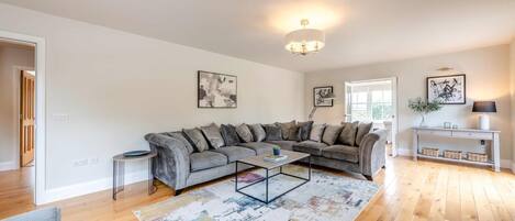 A modern living room with a grey sectional sofa, a coffee table, a console table with baskets, and a chandelier.