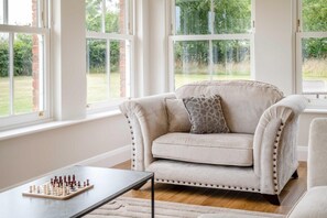 Ein Wohnzimmer mit einem beigen Sofa, einem Schachbrett und großen Fenstern.
