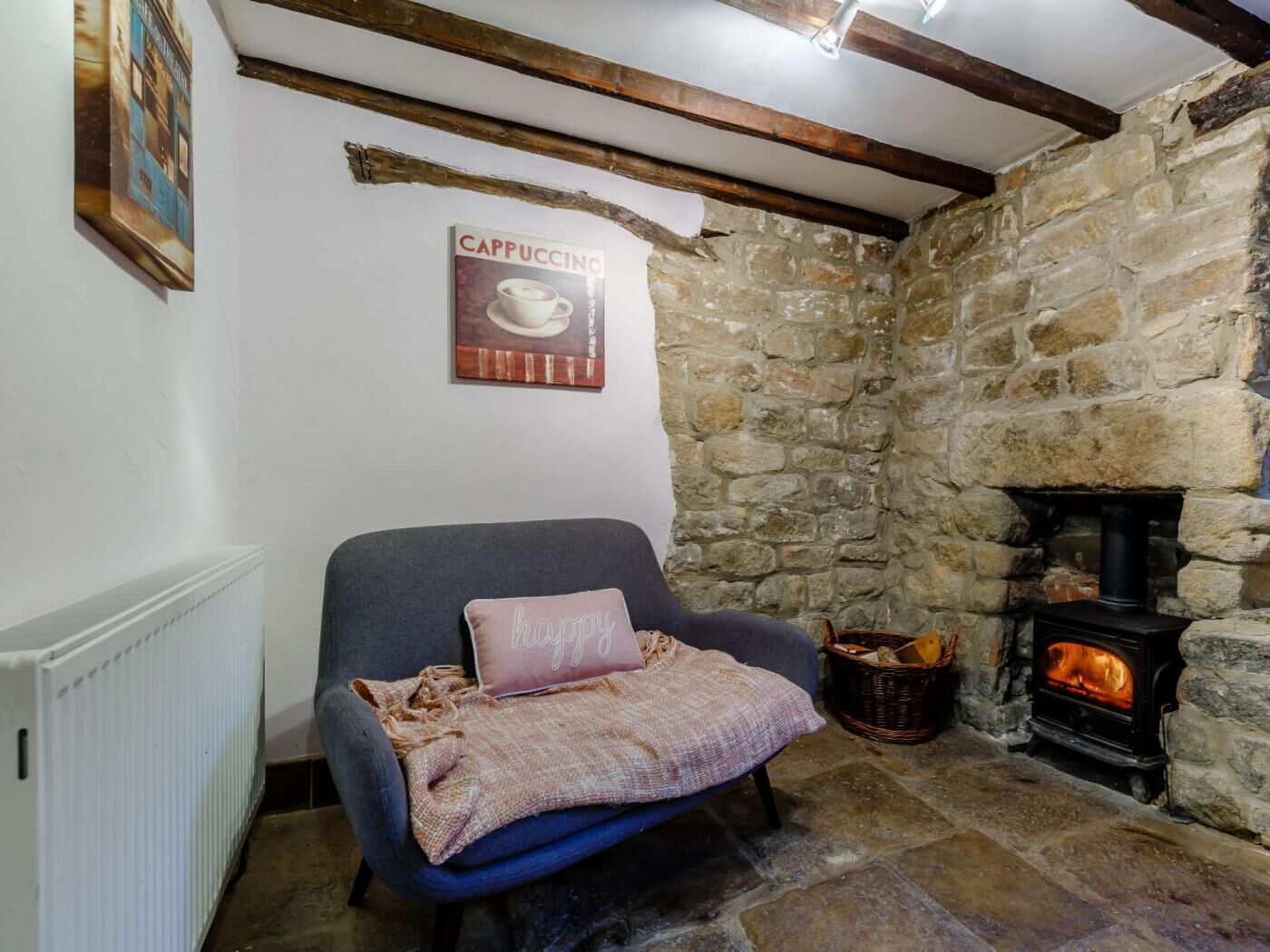 Une pièce chaleureuse avec un mur en pierre, une cheminée, un fauteuil bleu et une affiche accrochée au mur.