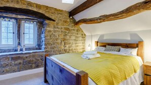 Una camera da letto con parete in pietra, travi in legno, un letto con copripiumino giallo e una finestra con due oggetti decorativi.
