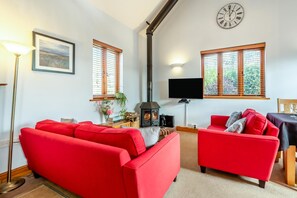 A living room with red sofas, a fireplace, a flat-screen TV, and a clock on the wall. - 3 Bed in Bideford (oc-86046) (Hartland)