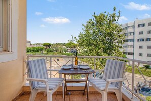 Ein Balkon mit zwei gestreiften Stühlen, einem kleinen Tisch und einer Weinflasche.
