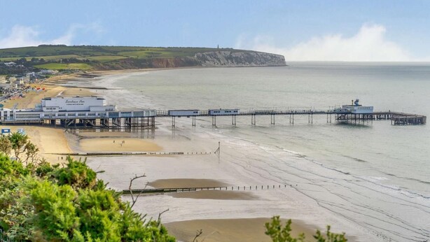 A coastal scene with a pier extending into the sea, a beach, and a cliff in the background. - 3 Bed in Sandown (oc-85985) (Sandown)