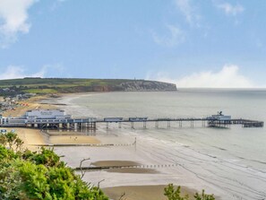 Un paysage côtier avec une jetée qui s’avance dans la mer, une plage et une falaise en arrière-plan.
