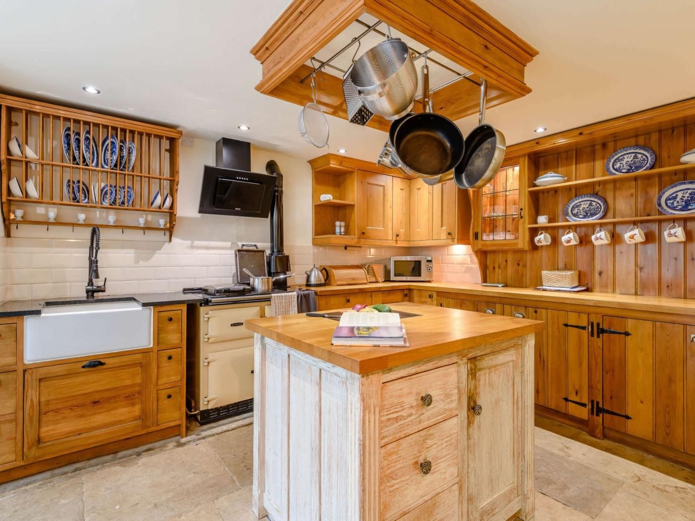 Une cuisine avec des meubles en bois, un îlot central, des ustensiles de cuisine suspendus et un four à micro-ondes.
