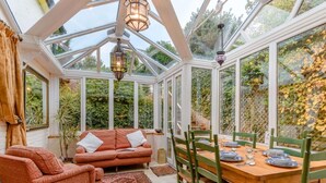 A conservatory with a glass roof, a wooden dining table, green chairs, a red sofa, and a patterned rug. - 3 Bed in Sandown (oc-85985) (Sandown)