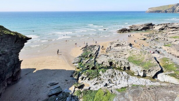 Une plage côtière avec un terrain rocheux et une eau d’un bleu limpide.