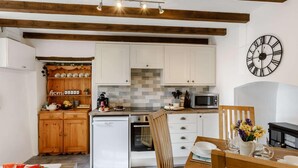 Une cuisine avec des meubles blancs, un four à micro-ondes, une machine à café et une table à manger en bois avec des chaises.