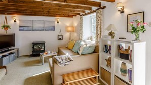 Un salon chaleureux avec des poutres apparentes, un téléviseur, une cheminée, un canapé et une bibliothèque.