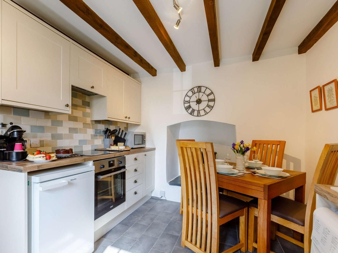 A compact kitchen with white cabinets, a microwave, and a wooden dining table with chairs.