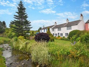Une maison traditionnelle avec un jardin, un ruisseau et un grand arbre.