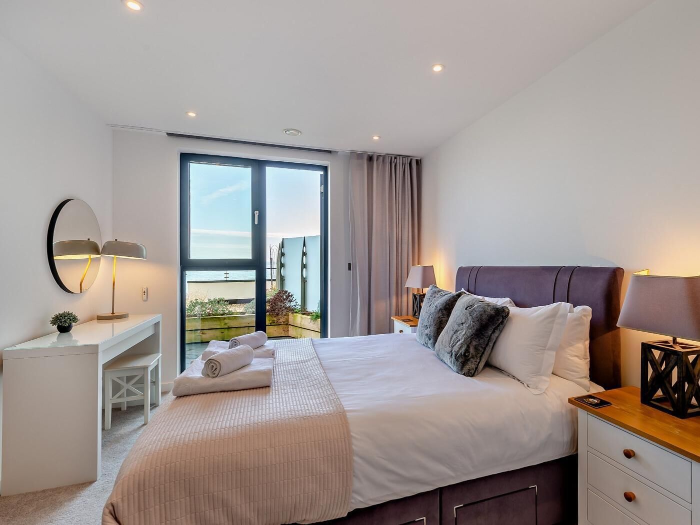 A hotel room with a bed, bedside tables, a desk, and a large window with a view.