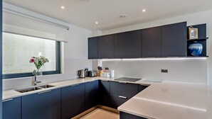 A modern kitchen with dark cabinets, a white countertop, and a window with a vase of flowers. - 2 Bed in Ramsgate (oc-86126) (Ramsgate)