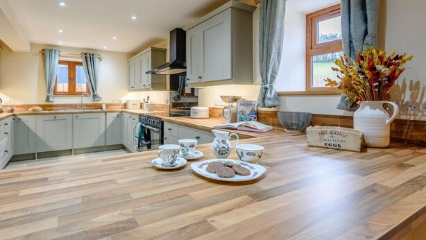 A kitchen with a wooden countertop, a stove, and a window with curtains. - 4 Bed in Llandrindod Wells (oc-86118) (Llaithddu)