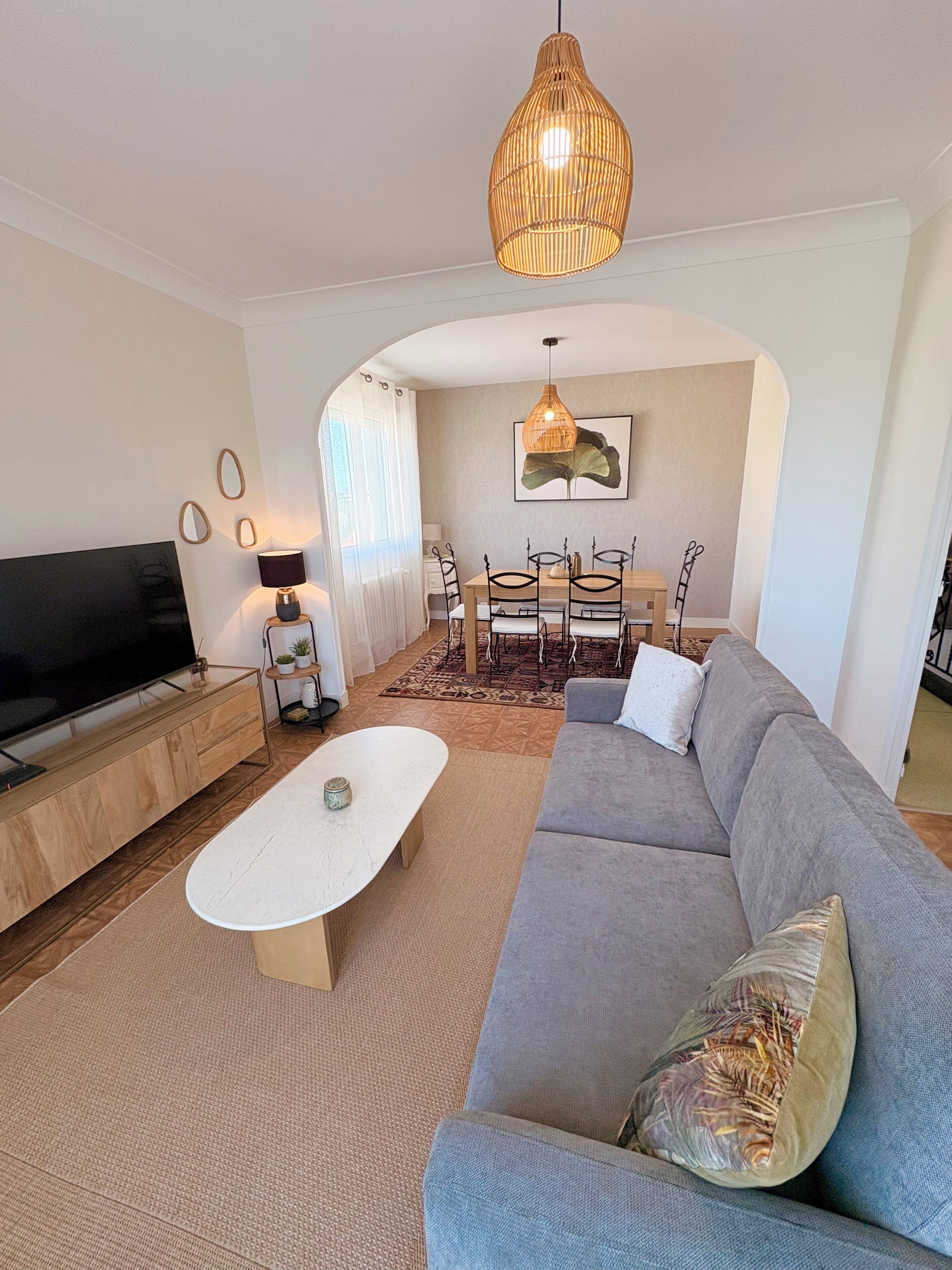 A modern living room with a sofa, TV, coffee table, dining table, and a hanging light fixture.