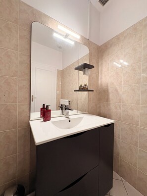 Een badkamer met een wit wastafelmeubel, donkere kastjes, een spiegel en een plank met toiletartikelen.