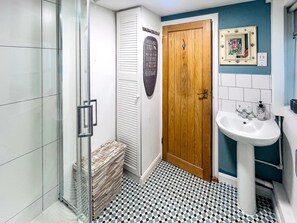 Un bagno con cabina doccia in vetro, una porta in legno, un lavandino bianco e un pavimento piastrellato.