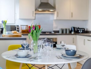 Een eettafel gedekt voor vier personen, met een vaas tulpen, een koffiezetapparaat en een magnetron op de achtergrond.