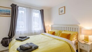 Habitación de hotel con cama, lámparas de noche, mesita de noche, ventana con cortinas y un cuadro en la pared.