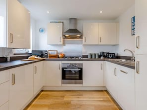 A modern kitchen with white cabinets, stainless steel appliances, and a wooden floor. - 2 Bed in Y Felinheli (oc-86260) (Y Felinheli)