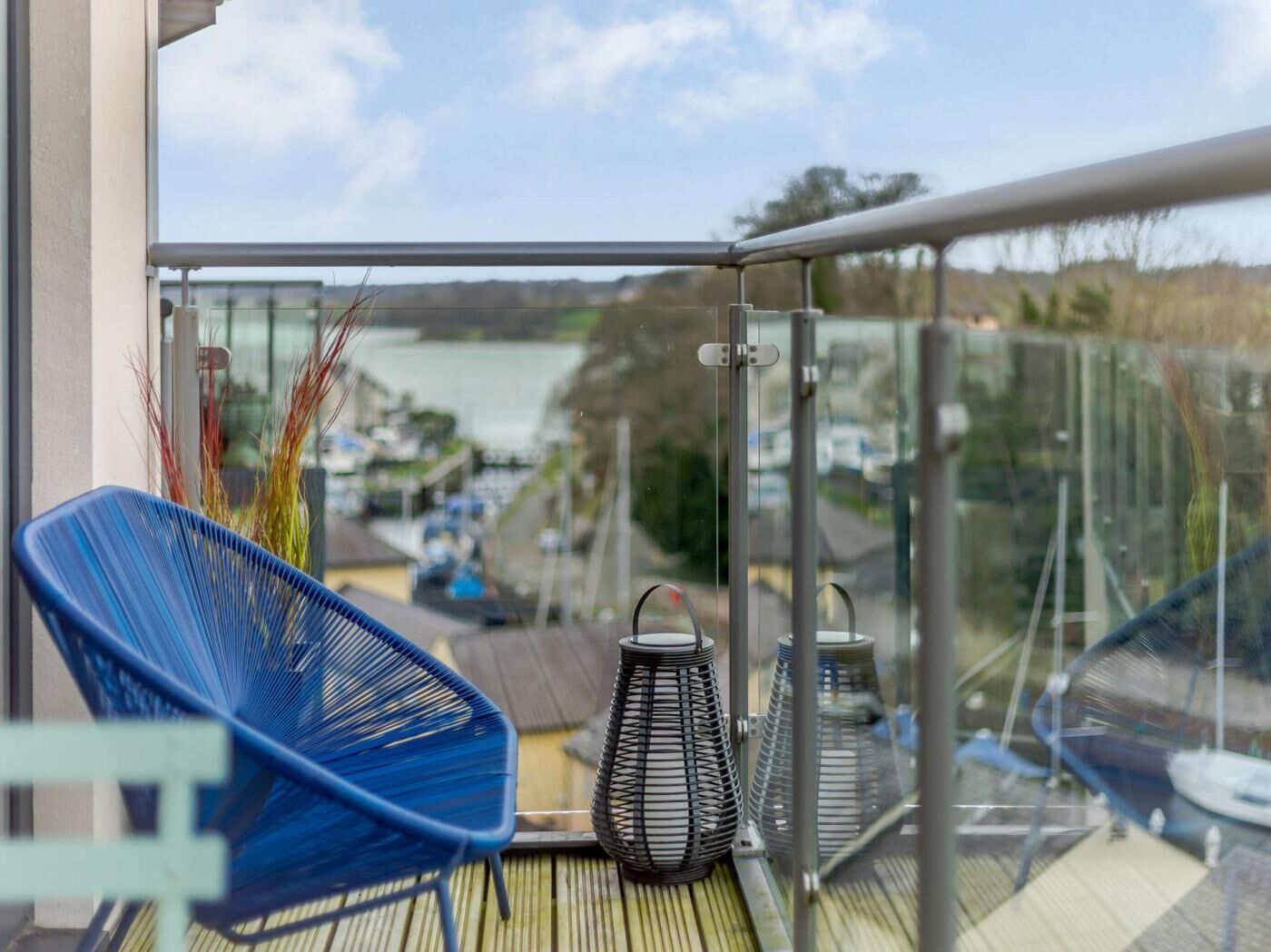 Un balcon donnant sur une étendue d’eau, une chaise bleue et deux lanternes en métal.