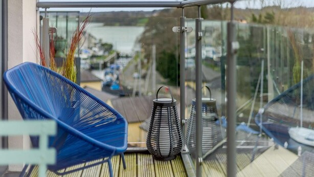 Un balcón con vista a una masa de agua, una silla azul y dos faroles metálicos.