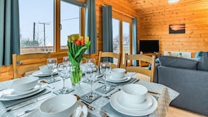 A wooden cabin interior with a dining table set for four, a sofa, and a TV.