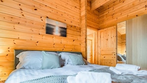 A wooden cabin room with a bed, pillows, a blanket, and a painting on the wall.