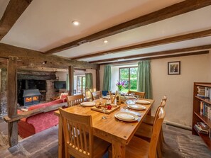 A rustic dining room with a wooden table set for four, a fireplace, and a bookshelf. - 4 Bed in Hereford (oc-86497) (Llanveynoe)