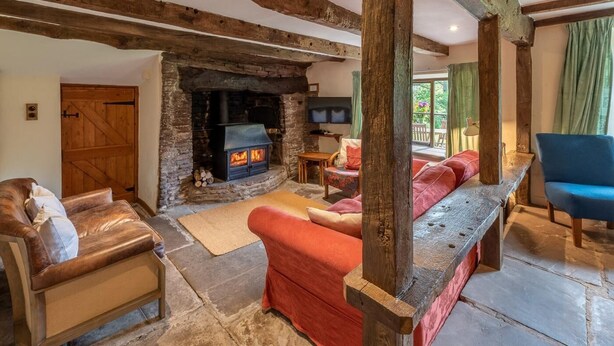 Ein rustikales Interieur mit sichtbaren Holzbalken, einem Kamin aus Stein, Ledersofas und einem Fernseher.