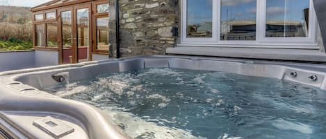 A hot tub with a stone wall and windows.
