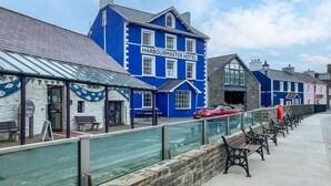 Ein blaues Gebäude mit dem Schriftzug 'Harbourmaster Hotel', einem überdachten Sitzbereich und Steinmauern.