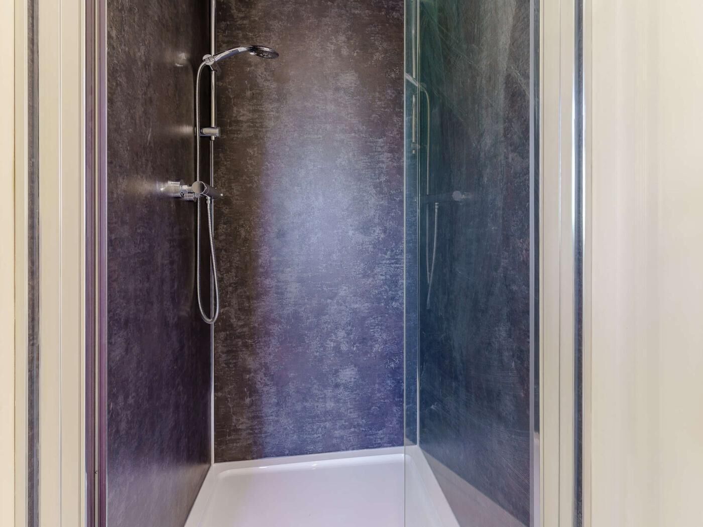 A shower enclosure with a glass door, a handheld showerhead, and a wall-mounted faucet.