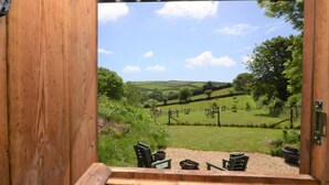 A wooden-framed window with a view of a grassy landscape and a seating area with chairs and a table. - 1 Bed in Kingsbridge (oc-86462) (Kellaton)