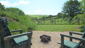 A view from a deck with two green chairs facing a grassy field and hills in the distance. - 1 Bed in Kingsbridge (oc-86462) (Kellaton)