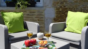 Un área de estar exterior de mimbre con cojines, una mesa con manzanas, un bol de fruta y copas de vino.