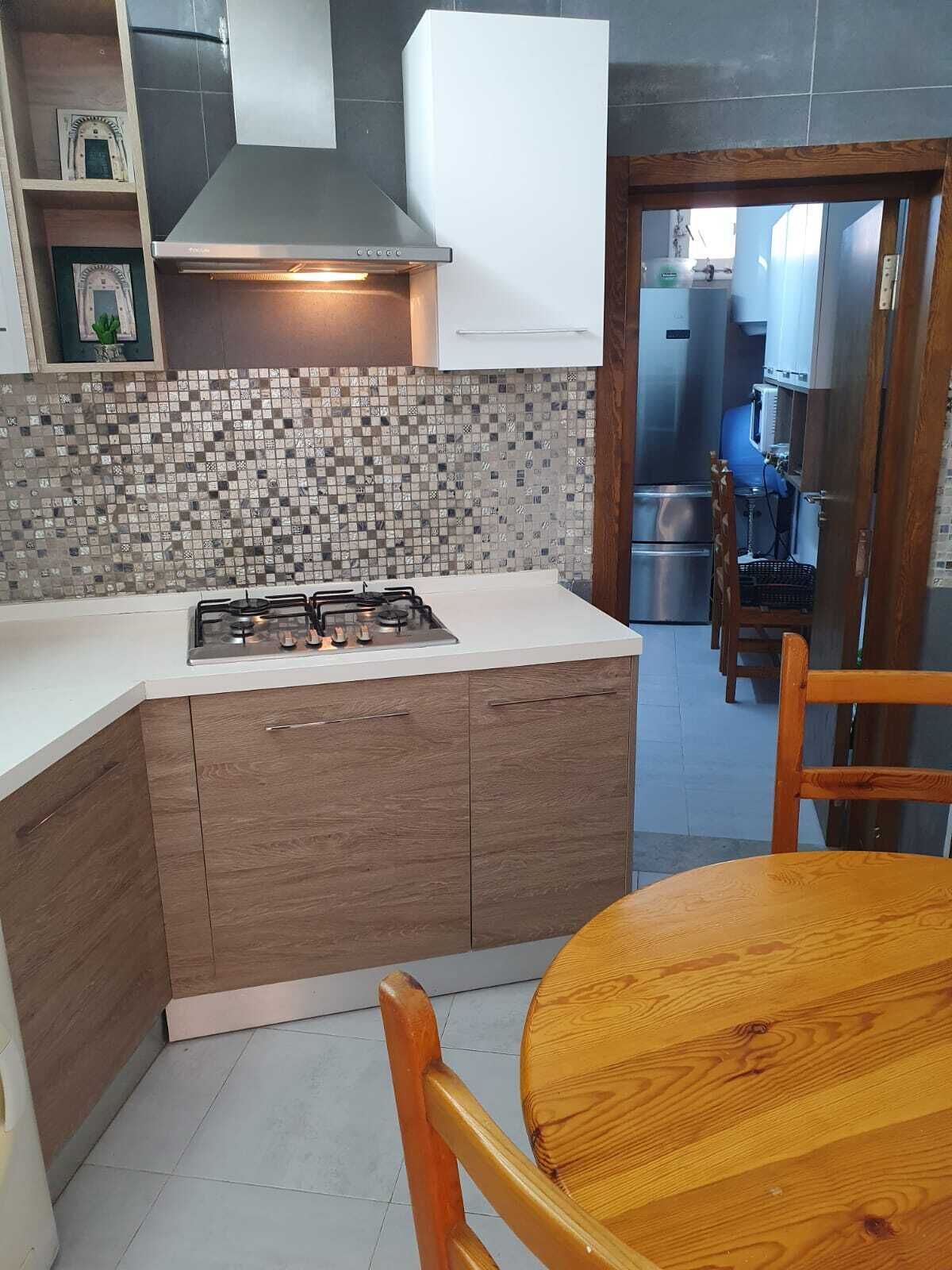 A modern kitchen with a gas stove, wooden cabinets, a tiled backsplash, and a dining area with a wooden table and chair.