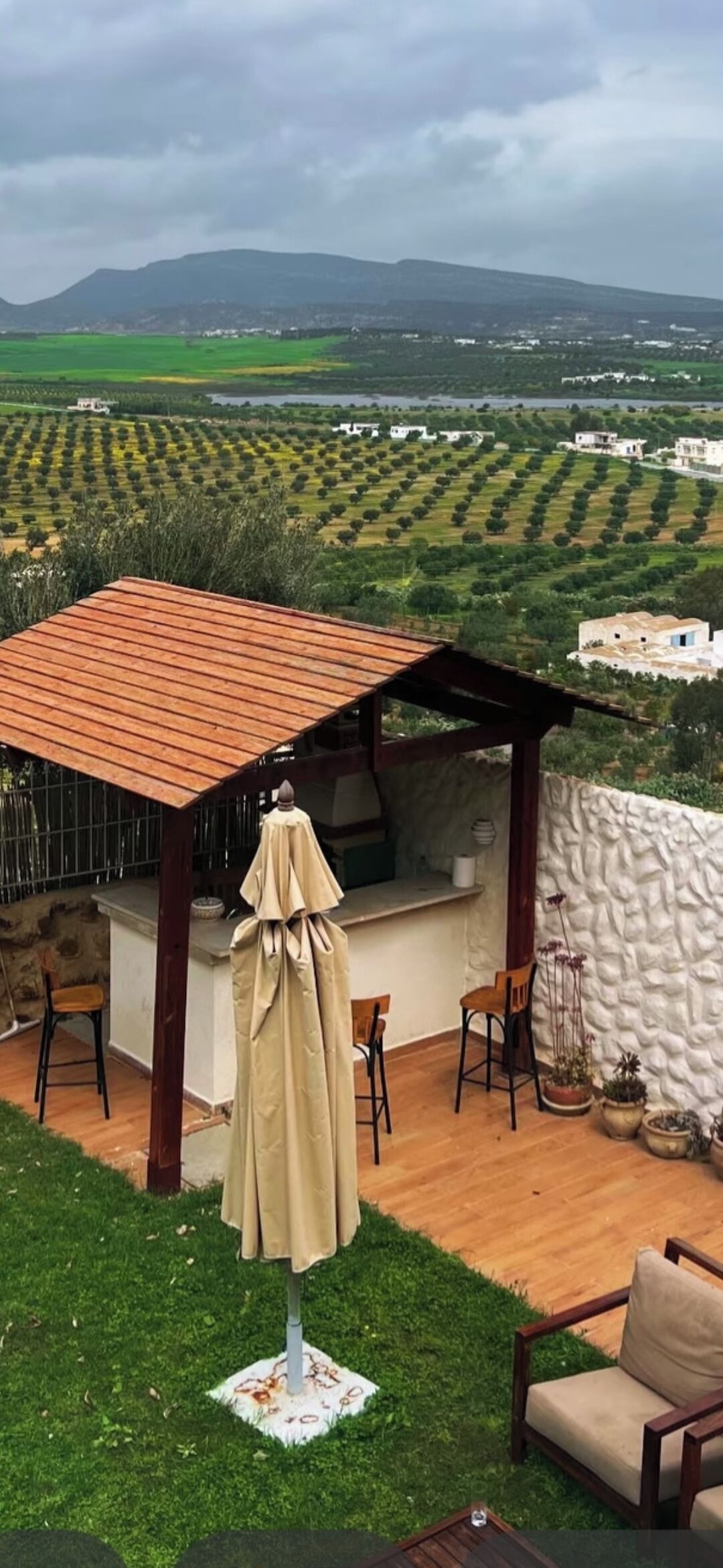 Ein überdachter Außenbereich mit Tisch und Stühlen, einer kleinen Küche und Blick auf einen Weinberg.