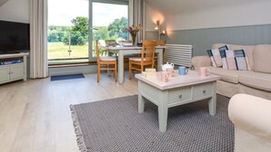 Ein modernes Wohnzimmer mit Fernseher, Esstisch, Stühlen, einer Couch und Blick auf Grünflächen.