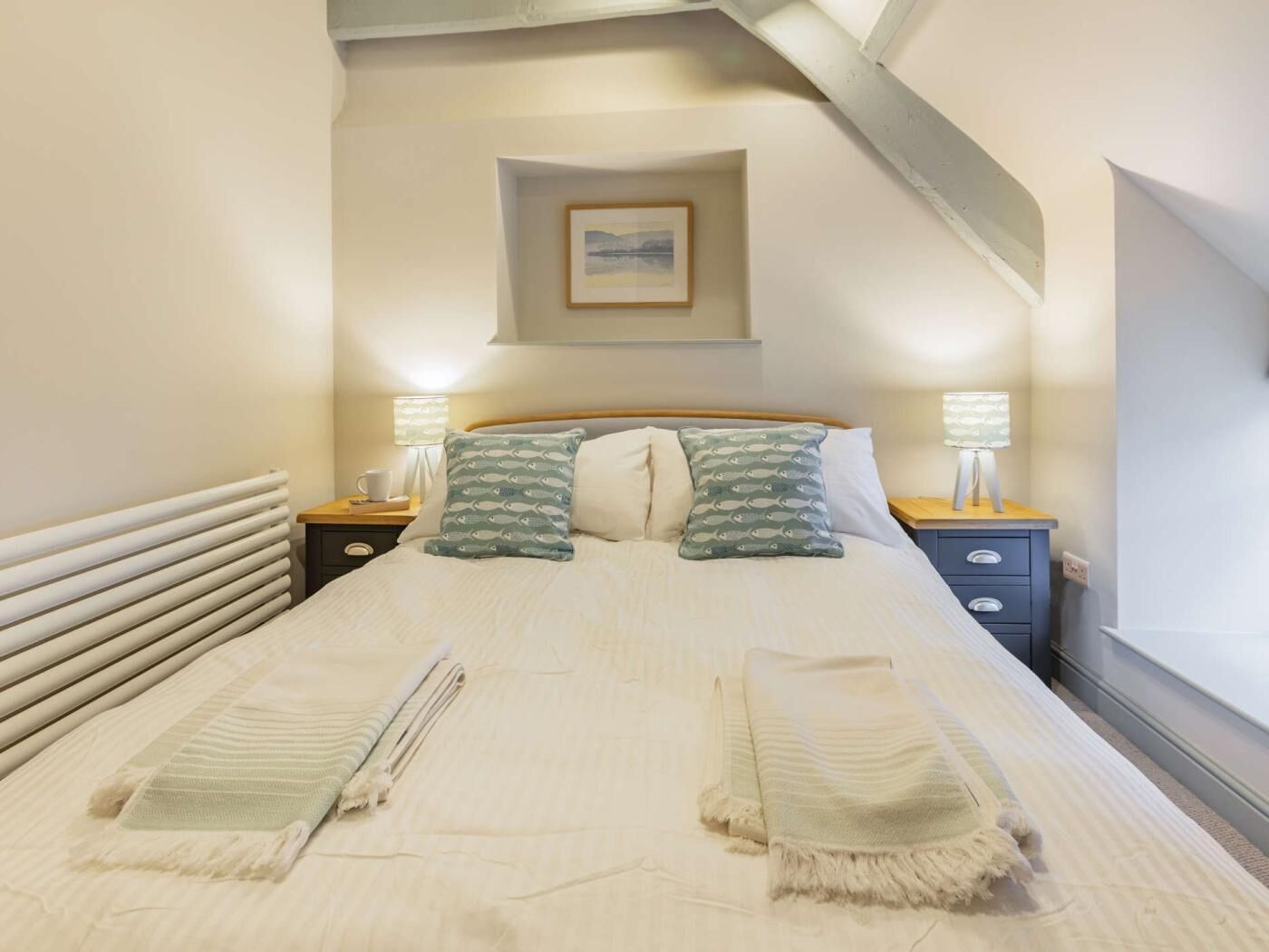 A bedroom with a bed, two bedside tables, a nightstand, a framed picture on the wall, and a window.