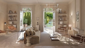 Ein großzügiger Wohnraum mit einer großen Couch, einem Couchtisch und einem Essbereich mit einem Metalltisch und Stühlen. Es gibt Bücherregale mit Büchern und Dekoration, und es gibt einen Blick auf einen Garten durch die offenen Türen.