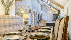 A dining area with a long table set for a meal, a sofa, and a stone wall in the background. - 8 Bed in Bridgend (oc-86493) (Southerndown)